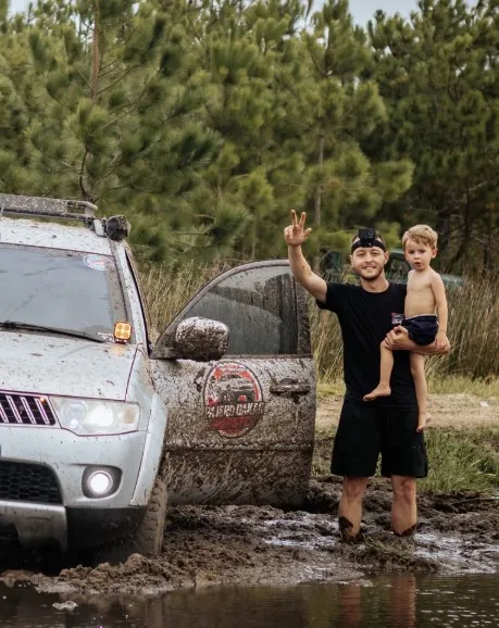 Rafael Polipo com o filho no colo, na lama, ao lado da Pajero